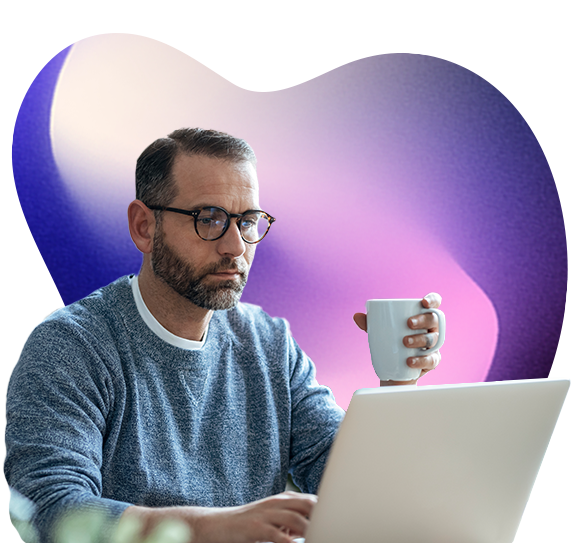 A man holds a cup in one hand while reading something on a laptop screen
