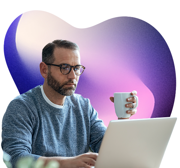 A man holds a cup in one hand while reading something on a laptop screen