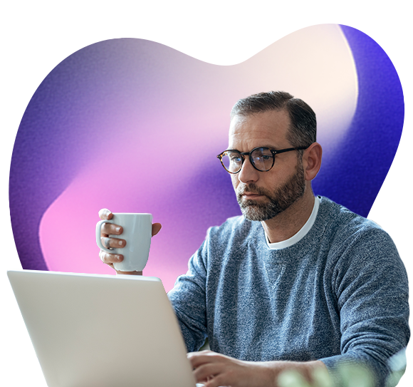 A man holds a cup in one hand while reading something on a laptop screen