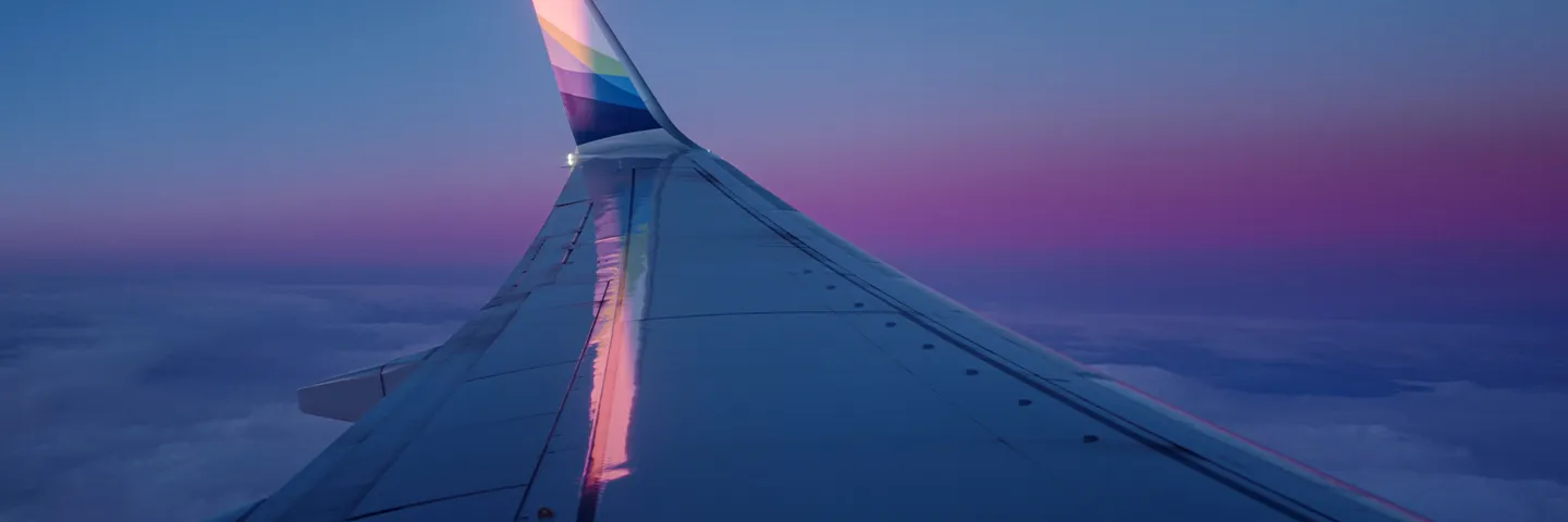 A view along a plane's wing, with an upswept tip, against a blue/purple evening sky