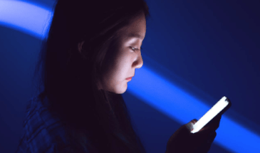 A lady in a dark room looks at a mobile device screen